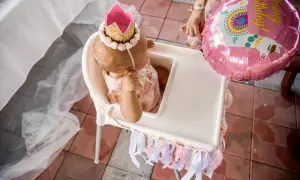 Mała księżniczka w koronie świętuje swoje 1 urodziny. Obok różowy balon z lamą.