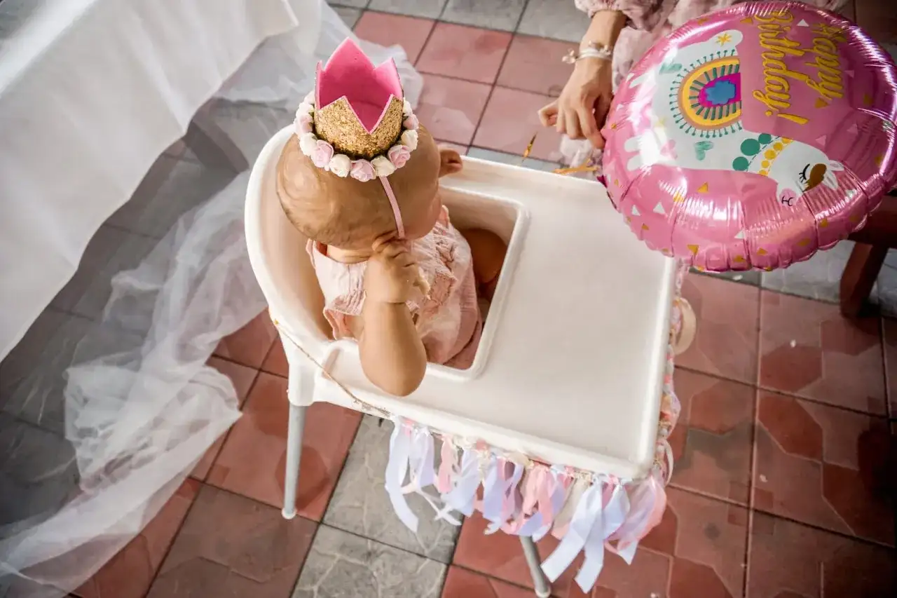 Mała księżniczka w koronie świętuje swoje 1 urodziny. Obok różowy balon z lamą.