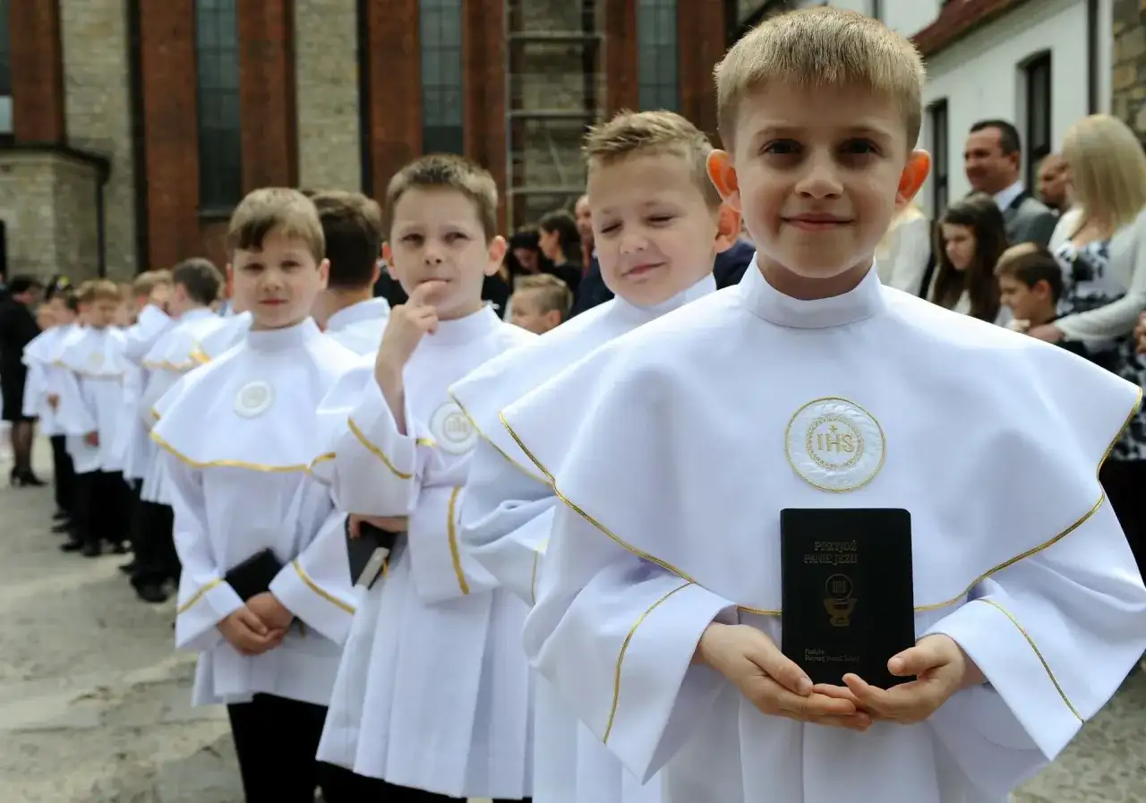 Chłopcy w albach komunijnych, jeden trzyma modlitewnik. To ważny dzień, gdy dziecko musi umieć do pierwszej komunii.