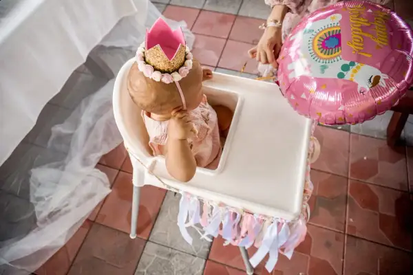 Mała księżniczka w koronie świętuje swoje 1 urodziny. Obok różowy balon z lamą.
