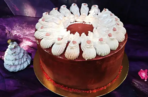 Elegancki tort w domu, ozdobiony bitą śmietaną i serduszkami. Obok stoi porcelanowa laleczka w sukni.