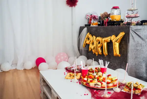 Złote balony z napisem "PARTY" i przekąski na stole tworzą atmosferę wieczoru panieńskiego w domu.