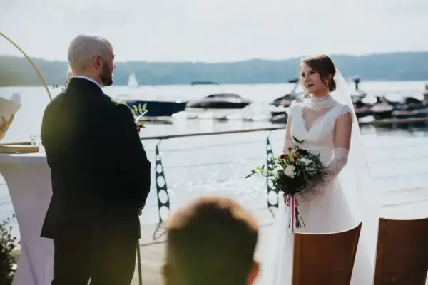 Para młoda podczas ślubu rzymskiego nad jeziorem. Panna młoda w białej sukni z bukietem, pan młody w garniturze.