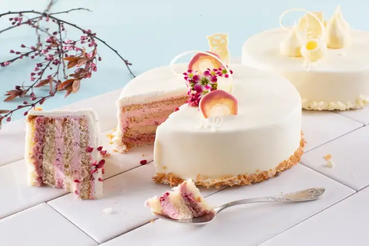 Delikatne torty z różowym kremem i owocami. Widoczne jakie warstwy do tortu, ozdobione białymi czekoladowymi figurkami i kwiatami.